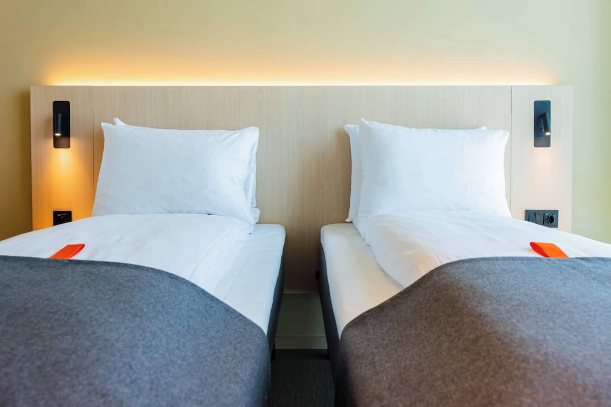 A hotel room with two beds, each with white linens and grey throw pillows.
