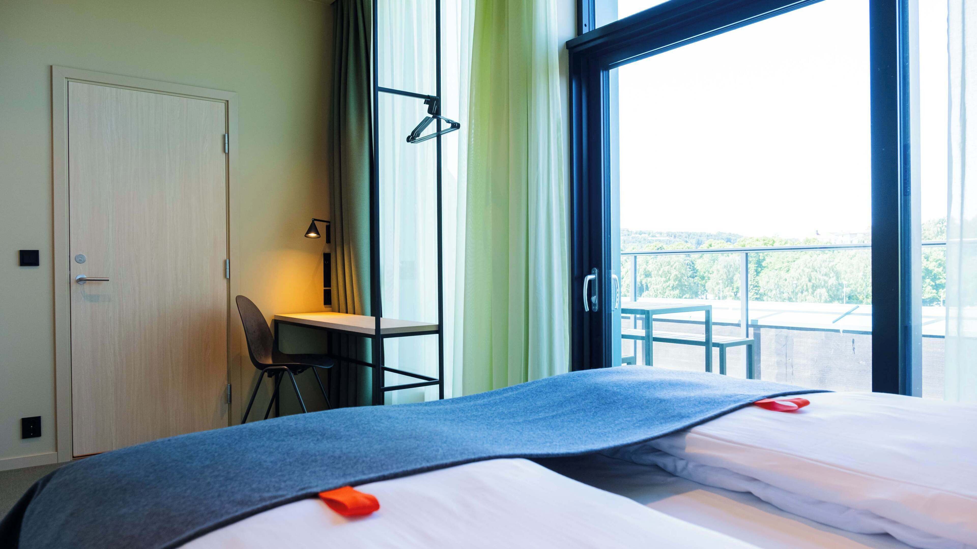 Hotellihuone, jossa on sänky, työpöytä, tuoli ja näkymä parvekkeelle.