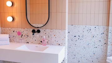 Ein Badezimmer mit weißem Waschbecken, einem beleuchteten Spiegel und Wänden mit punktierten Fliesen.