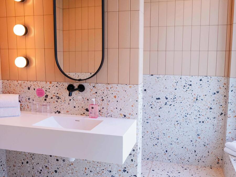 Ein Badezimmer mit weißem Waschbecken, einem beleuchteten Spiegel und Wänden mit punktierten Fliesen.