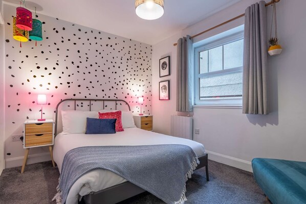 Un dormitorio con cama, mesitas de noche, una ventana con cortinas y una pared con diseño.