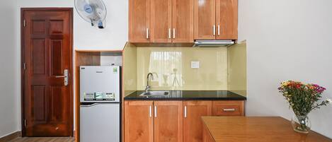 A compact kitchen with wooden cabinets, a refrigerator, a sink, and a dining table.