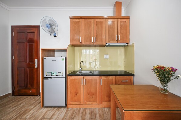 Una cocina compacta con armarios de madera, un refrigerador, un lavamanos y una mesa de comedor.