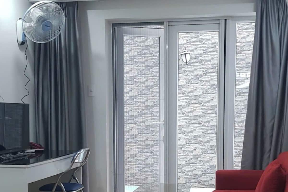 Un salon moderne avec un plancher en bois, un canapé rouge, une petite table, un bureau avec un ordinateur et une grande fenêtre avec des rideaux.