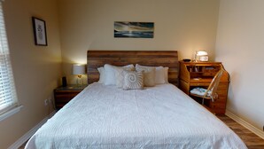 A neatly arranged bedroom with a large bed, a wooden headboard, a nightstand with a lamp, a small desk, and a chair. - FH4, Near Beach, Shared Pool, Golf Cart Access (Port Aransas)