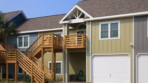 A two-story house with a wooden staircase leading to a balcony, a garage, and a small garden area. - FH4, Near Beach, Shared Pool, Golf Cart Access (Port Aransas)