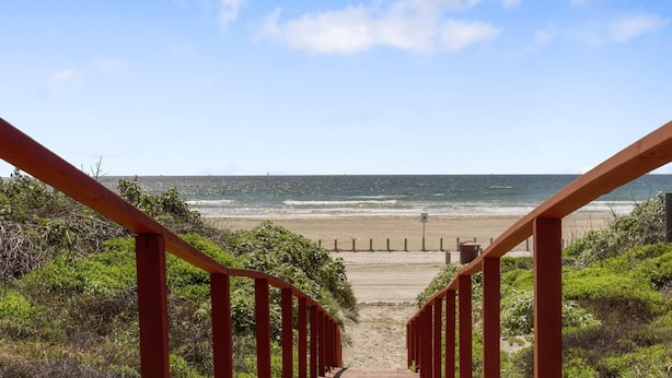 Un escalier menant à une plage d’où l’on a une vue dégagée sur l’océan.