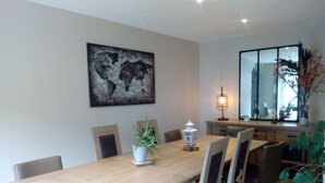 A dining area with a wooden table, six chairs, a world map artwork, a potted plant, and a lamp.