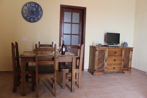 A dining area with a wooden table and chairs, a clock on the wall, a cabinet with drawers, and a television on a stand.
