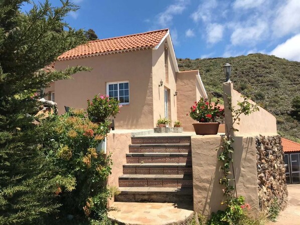 A two-story house with a red-tiled roof, a stone staircase, and potted plants.