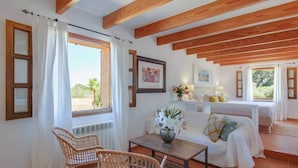 A room with a bed, two wicker chairs, a table with a vase, and a window with curtains. - Dream finca: XXL pool, table tennis, BBQ house, volleyball, air-condition (Port de Pollença)
