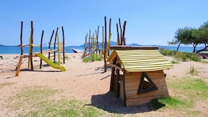 A beach with wooden play structures, including a slide and climbing frames, and a small wooden hut with a striped awning. - Dream finca: XXL pool, table tennis, BBQ house, volleyball, air-condition (Port de Pollença)