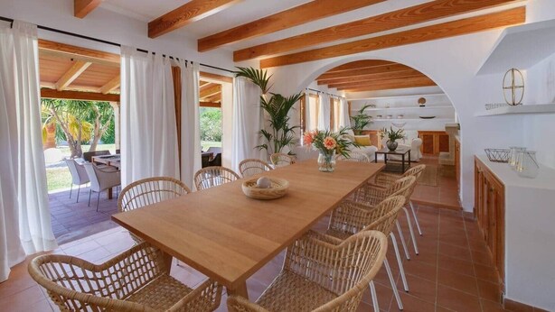 A dining area with a wooden table and wicker chairs, an open kitchen with white cabinets, and a view of the outdoors. - Dream finca: XXL pool, table tennis, BBQ house, volleyball, air-condition (Port de Pollença)