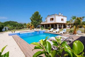 Eine Villa mit Swimmingpool, Liegestühlen und einem Garten.