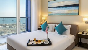 A hotel room with a large bed, a city view, a painting, and a tray with breakfast.