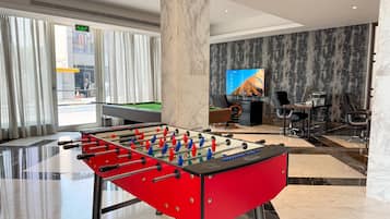 A modern hotel lobby with a foosball table, a pool table, and a television on the wall.