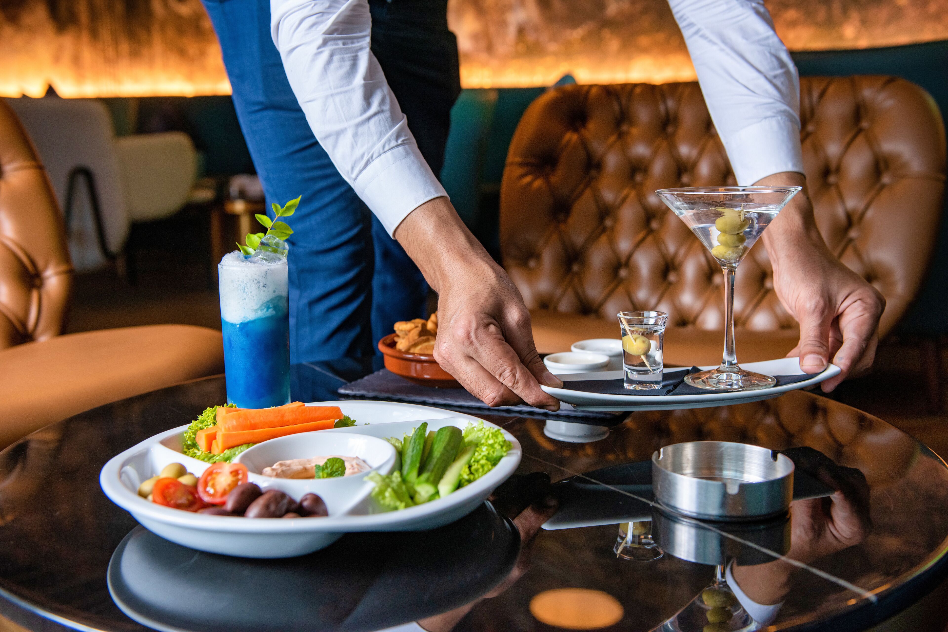 Une personne qui sert des plats et des boissons sur un plateau à une table dans un restaurant.