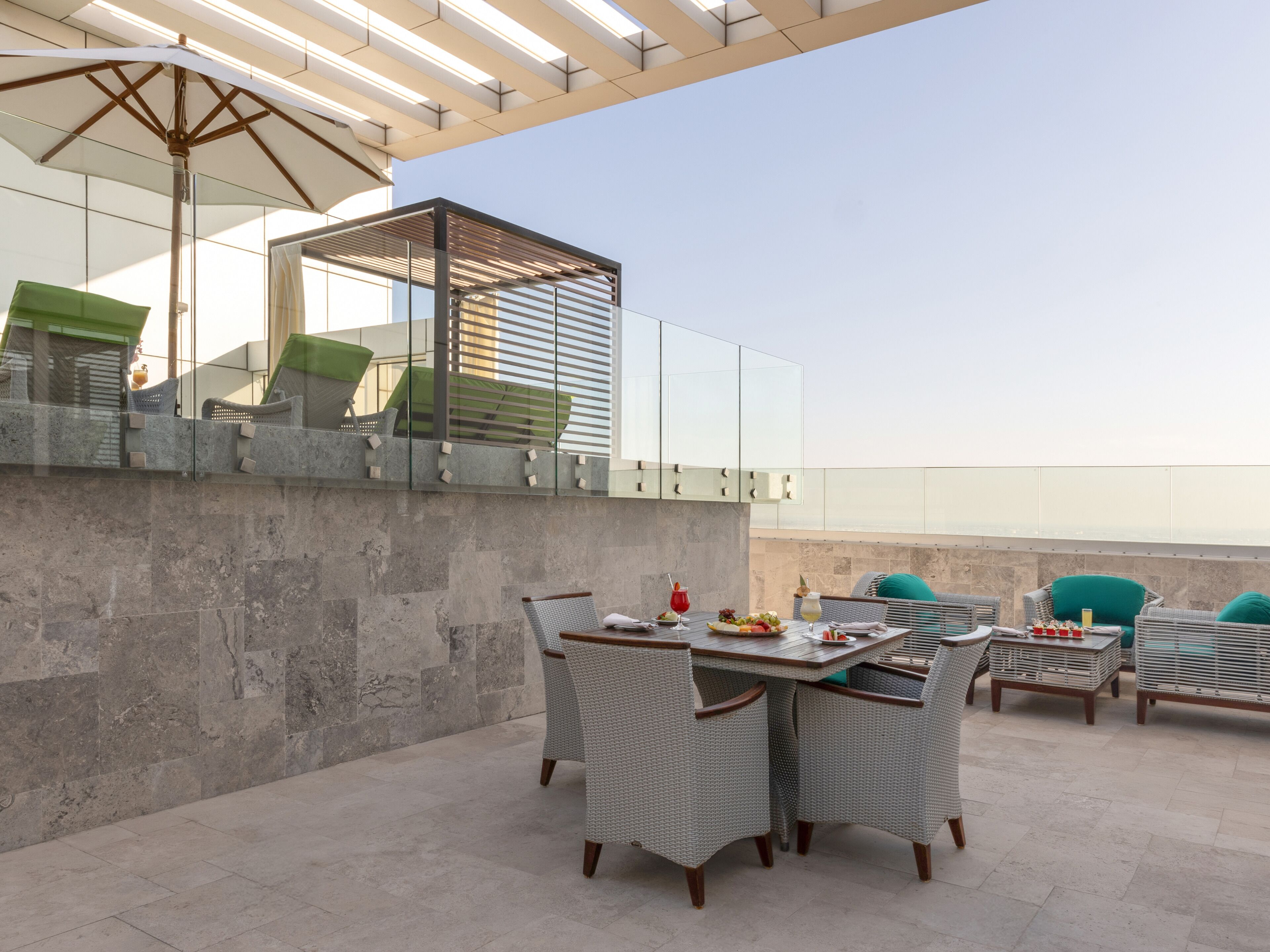 An outdoor patio with wicker furniture, a glass table, and a view of the sea.