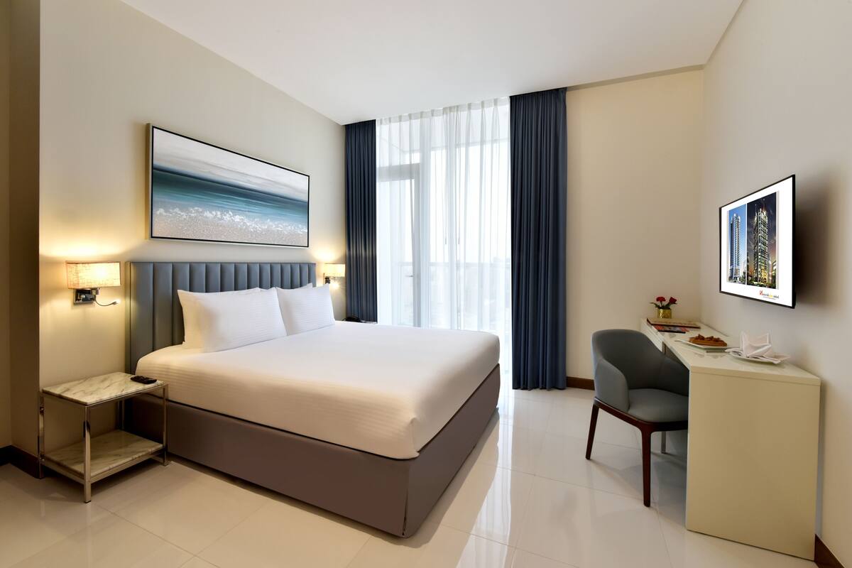 A modern hotel room with a large bed, bedside tables, a desk, and a chair.