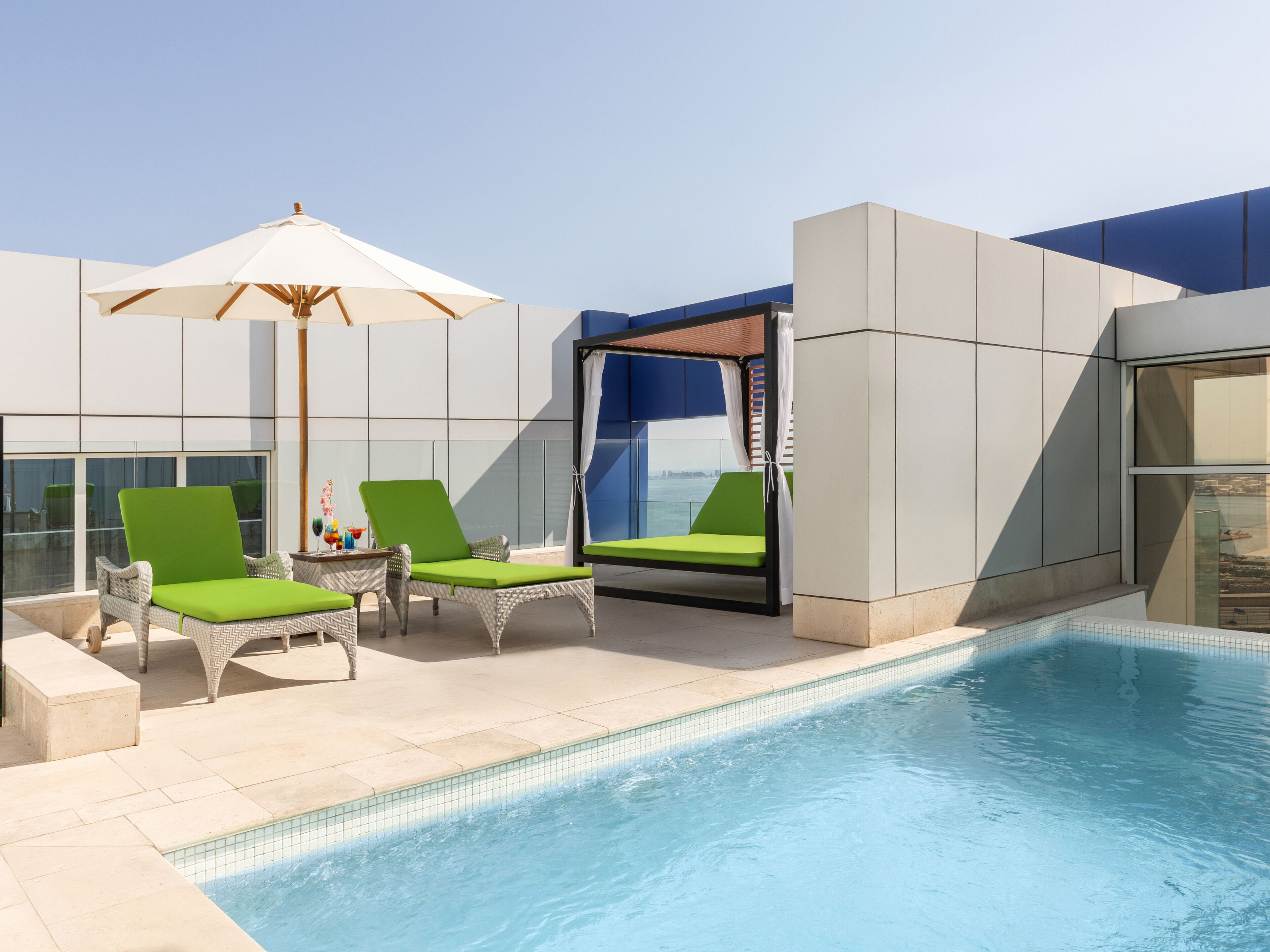 A modern outdoor pool area with lounge chairs and a large umbrella.