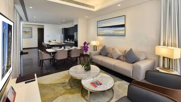 A modern hotel room with a sofa, two round coffee tables, a dining area, and a kitchen.