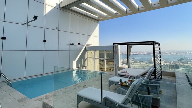 A rooftop pool area with lounge chairs and a glass balustrade overlooking a cityscape.