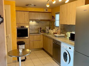 A compact kitchen with wooden cabinets, a built-in oven, a washing machine, and a small round table. - Vacation house 2 bedrooms in Châtelaillon-Plage (Châtelaillon-Plage)