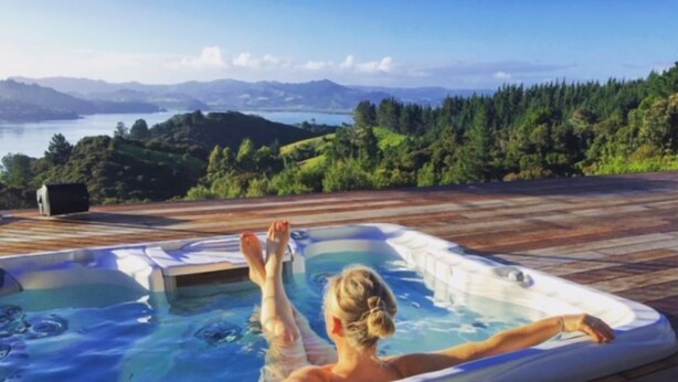 Une personne se détend dans un bain à remous, avec une vue panoramique sur un lac et des montagnes en arrière-plan.