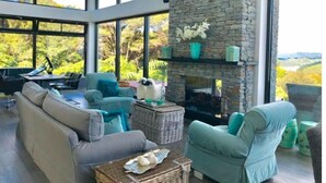 Un salon moderne avec une cheminée en pierre, de grandes fenêtres et une vue sur l’extérieur.