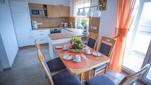 A modern kitchen with wooden cabinets, a microwave, and a dining area with a table set for four. - 4****Sterne Spatzennest 86 sqm between Augsburg and Ulm quietly located new building (Burtenbach)