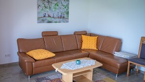 A brown leather sofa with yellow cushions, a wooden coffee table with a white cloth, and a painting of birds on a branch. - 4****Sterne Spatzennest 86 sqm between Augsburg and Ulm quietly located new building (Burtenbach)