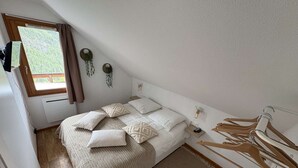 Une chambre à coucher avec un lit, une fenêtre, une plante suspendue et un plancher en bois.
