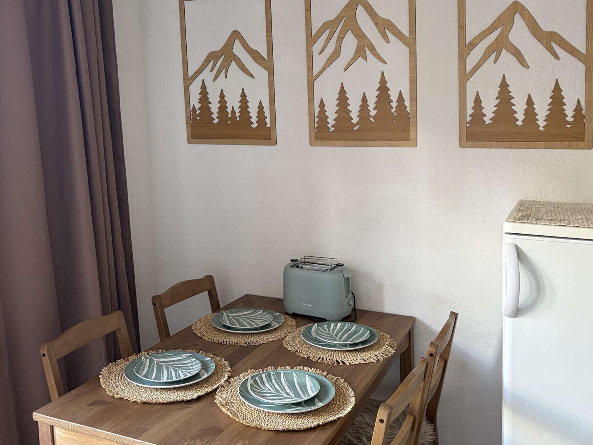 Een eettafel met vier borden, een broodrooster en een koelkast.