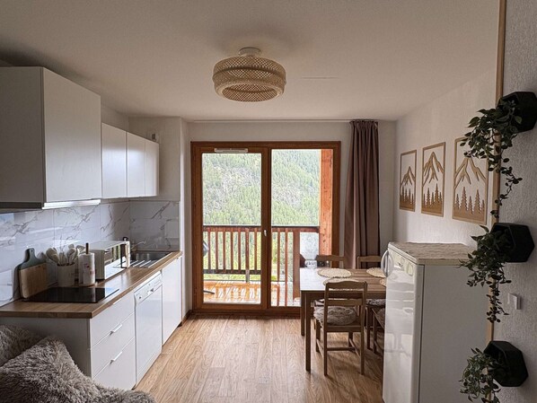 A compact kitchen with a dining area, wooden flooring, and a view through a sliding glass door.