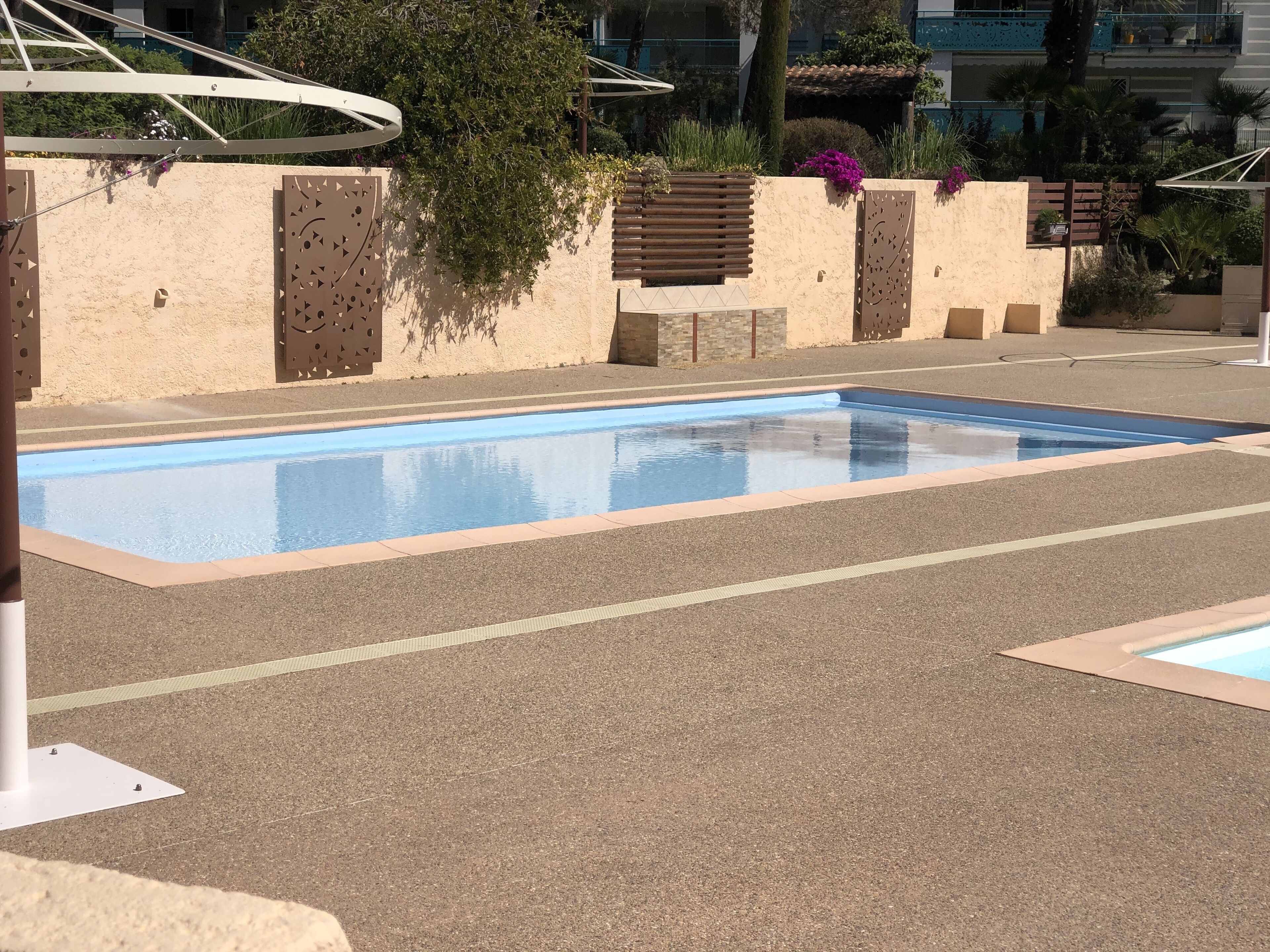 A swimming pool with a clear blue water surface, surrounded by a paved area with a beige wall and decorative panels.