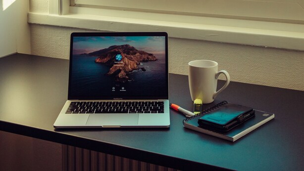 A laptop on a desk by a window with a view of trees and a body of water. - Lövudden Strand (Vasteras)