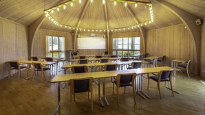 A large, naturally lit room with wooden walls and ceiling, featuring multiple tables and chairs arranged for group gatherings. - Lövudden Strand (Vasteras)