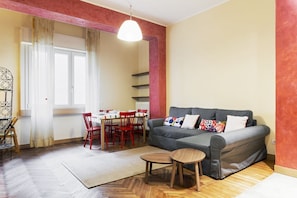 Un salon comprenant un canapé, une table à manger avec des chaises, une petite table en bois et un luminaire suspendu.