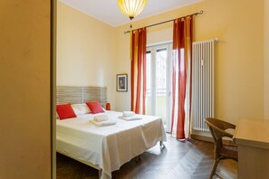 A hotel room with a bed, a chair, a table, and a window with curtains.