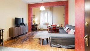 A living room with a sofa, TV, dining table, chairs, and a wooden floor. - Hostmate - Milano - Sapeto- Colonne S.Lorenzo (Milano)