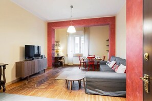 A living room with a sofa, TV, dining table, chairs, and a wooden floor.