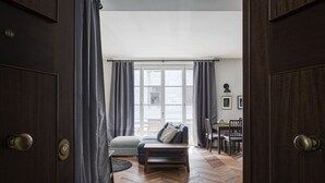 Een kamer met een visgraatvloer, een bank, een kleine tafel en een eethoek met stoelen.