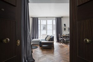 Une pièce avec un parquet en chevrons, un canapé, une petite table et un coin repas avec des chaises.