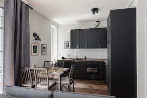A modern kitchen with dark cabinets, a dining table with chairs, and a sofa in the foreground.