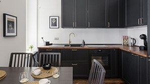 Een moderne keuken met donkere kastjes, een houten aanrechtblad, een ingebouwde oven en een spoelbak met een gouden kraan.