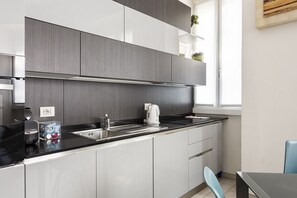 A modern kitchen with grey cabinets, a black countertop, a kettle, and a sink.