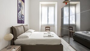 Quarto moderno com cama, mesa de cabeceira, abajur e obra de arte.