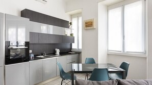 Uma cozinha moderna com armários cinzentos, bancada preta e área de jantar com mesa e cadeiras.