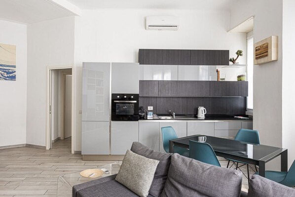 A modern kitchen with grey cabinets, a black countertop, and a dining area with a glass table and blue chairs.