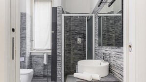 A modern bathroom with a white toilet, a glass-enclosed shower, a round sink, and a marble-tiled shower wall. - Hostmate - Milano - Filzi - Stazione Centrale (Milano)